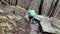 Rear view of young woman in raincoat descending carefully on rocky terrain. Female tourist overcomes obstacles in hike.