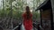 Rear View of Young Woman in Red Dress Walks Along Wooden Path Among Green Trees