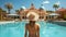 Rear view of young woman in straw hat standing near swimming pool
