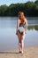 Rear view of young woman wearing khaki one-piece swimsuit standing on beach at bathing lake