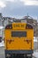 Rear of a yellow school bus against snowy homes and cloudy sky in winter