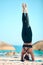 Rearview beautiful woman practising yoga exercise on the beach. Young female athlete doing a handstand or headstand