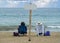 Rearview of a latin couple sitting on deck chairs at beach with a bamboo pole with a signboard in the middle of the beach chairs