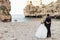 Rearview married romantic couple in wedding dress and suit stand on sea beach, contemplating. Vacaion and holiday event