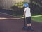 Rearview portrait Kid riding a roller on the road, Lonely schoolboy standing on scooter and looking down on the pathway, Sad