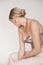 Rearview of posh blond woman in silver sparkling top and golden necklace, earrings accessories sitting in white studio