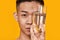 Rebalance. Portrait of young asian man looking at camera, holding a glass of water near his face isolated over yellow