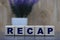 RECAP word on cubes on a gray background and lavender bush