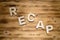 RECAP word made of wooden block letters on wooden board.