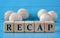 RECAP - word on wooden cubes on a blue background with wooden round balls