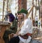 The reconstruction participant of the `Viking Village` sits with an ax and a goblet on the rock in the camp in the forest near Ben