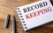 RECORD KEEPING text on notebook with pen on wooden background