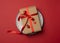 Rectangular brown cardboard box tied with a silk red ribbon lies in a round ceramic red plate