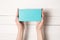Rectangular turquoise box in female hands. Top view. White table on the background