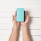 Rectangular turquoise box in male hands. Top view. White table on the background