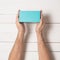 Rectangular turquoise box in male hands. Top view. White table on the background