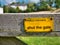 A rectangular, yellow, metal sign screwed to a wooden gate across a public footpath