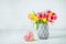 Recycled heart shape gift box with satin ribbon bow and spring bouquet of pink and yellow tulip flowers in a vase on the