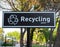 Recycling point sign ,words and symbol in white color on black background. Blurred public park on behind