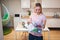 Recycling. Young smiling woman holding electronic waste in the container with green recycle icon on kitchen background