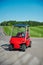 Red 2-seater golf electric cart on the paving road to a golf field