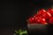 Red acerola cherries fruit in a ceramic bowl with a black background.