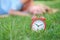 Red alarm clock on grass in background lies woman