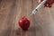 Red apple injecting a needle or syringe and chemical pesticides on a wooden background. Specific pesticide residues in apples,