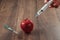 Red apple injecting a needle or syringe and chemical pesticides on a wooden background. Specific pesticide residues in apples,