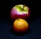 Red apple and tangerine on an ominous black background