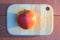 Red apple on a wooden board on red-brown table with a long blue shadow at sunset