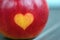 Red apples with a heart seal on the table. Orange heart on organically grown fruits. Growing fruits with prints. Close-up