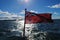 Red Australian flag on sunny day in the ocean with sail boat in back ground.