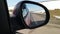 Red automobile in motion. View in the rear view side mirror of a auto, driving a red car along the track,