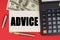 On a red background, among the money, a calculator and a pen lies a sign with the text - ADVICE