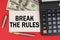 On a red background, among the money, a calculator and a pen lies a sign with the text - BREAK THE RULES