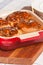 Red baking dish filled with freshly baked, homemade sticky buns covered in maple syrup