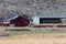 Red barn next to a hay metal hay barn in a field.