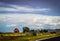 Red barn and outbuildings on farm along blacktopped highway with mountains in distance and pretty sky with fluffy clouds