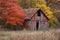 A red barn stands in a open field surrounded by trees under a blue sky, A dilapidated barn in an autumn setting, AI Generated