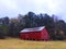 A red barn style building boarded up and abandoned distant view