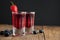 Red berries liqueur in shot glass isolated on black background and wooden table. Homemade alcohol drink concept.