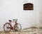 Red bicycle leaned to a white building with a window with rusty balusters