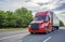 Red big rig long haul semi truck with black grille transporting cargo in dry van semi trailer running on the wide highway road
