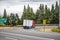 Red big rig semi truck with dry van semi trailer turning on the round highway exit with green trees on the side