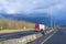 Red big rig semi truck with two semitrailers driving on divided multiline highway