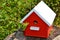 Red birdhouse with white roof, sitting on a log.