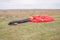 Red and black canopy paraglider lying on green grass against a cloudy sky background