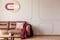 Red blanket and pink cushion on sofa in white apartment interior with poster and table.