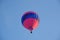 Red and blue hot air balloon seen from below against blue sky